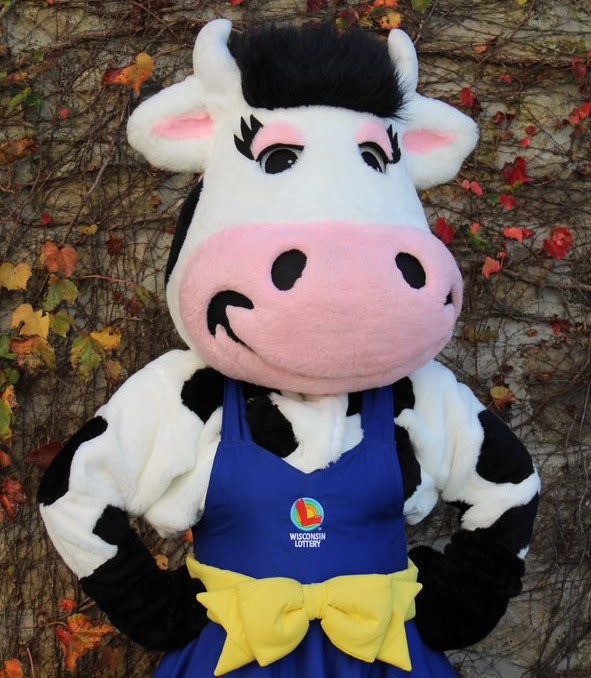 Wisconsin Lottery Moola Headshot picture of wisconsin lottery moola against brick building with vines moola is a cow mascot wearing a blue dress with a yellow bow