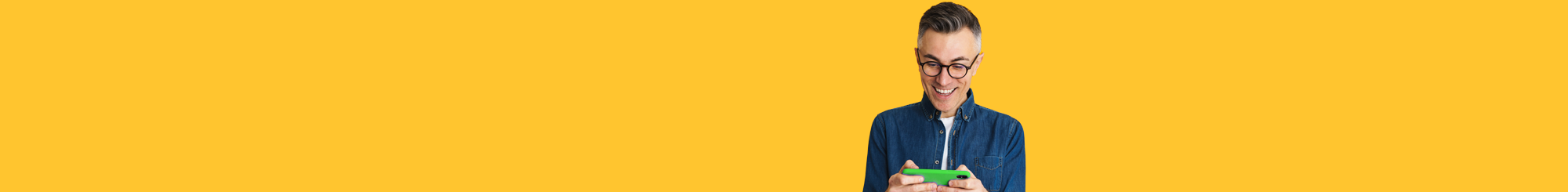 man in black glasses wearing blue jean button up and white t-shirt looking at green cell phone on yellow background